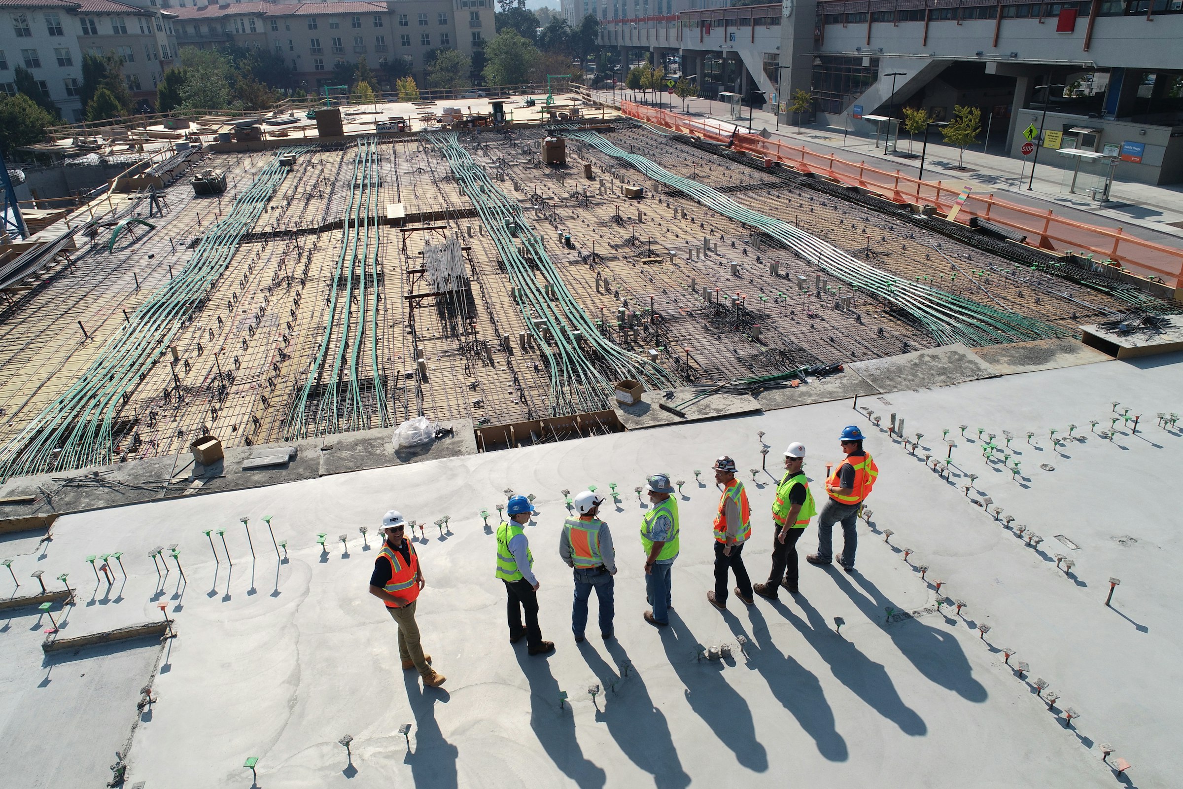A crew in hard hats and high-visibility vests walking a poured deck on an active construction site.
